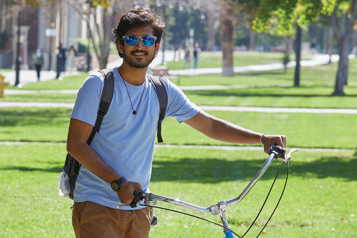 Student in sunglasses walking his bicycle