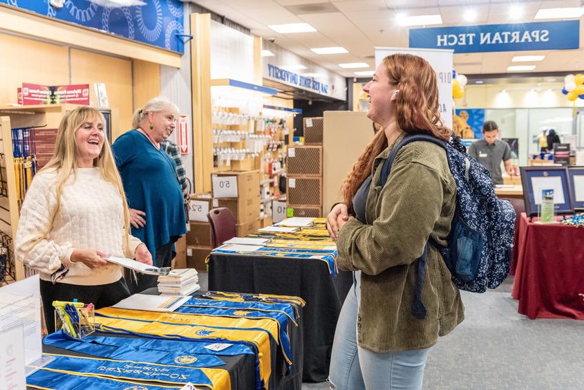 A student speaks with staff next to a table full of different stole styles.